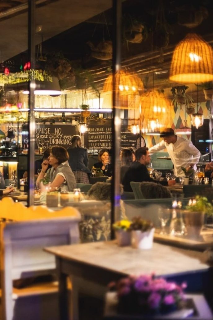 Belebtes Restaurantinterieur bei Nacht mit warm beleuchteten Rattanlampenschirmen und Gästen an Tischen.